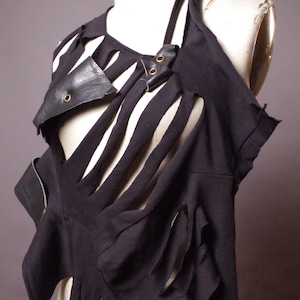 May include: Black sleeveless top with cut-out design and leather accents. The top features vertical slits and leather details around the neckline and shoulder. The garment is displayed on a mannequin.