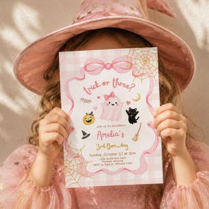 May include: A rectangular invitation card featuring a pink gingham background, a central pink ghost with a bow, a black cat, a pumpkin, and gold spiderwebs. The text reads: trick or three? JOIN US TO CELEBRATE Amelia's 3rd Boo_day Sunday, October 22 at 2pm.