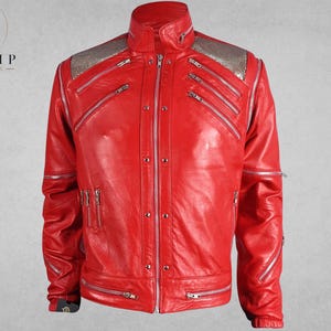 May include: A vibrant red leather jacket with silver zippers and accents. The jacket features a high collar, multiple zippered pockets, and silver shoulder detailing. The Trump Jackets logo is visible in the upper left corner.