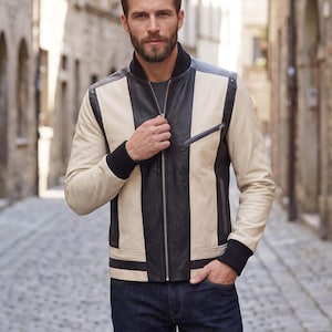 May include: A colour-blocked bomber jacket featuring vertical panels of black and cream leather. The jacket includes a central metal zip, a black ribbed collar, black ribbed cuffs, and a single zipped chest pocket on the left side.