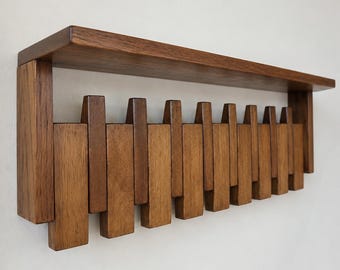 Könnte beinhalten: Ein wandmontiertes Holzregal mit einer Reihe vertikaler Holzlatten. Das Regal besteht aus dunkelbraunem Holz und hat eine rechteckige Form. Die Lamellen sind in einem versetzten Muster angeordnet und schaffen ein einzigartiges Design. Das Regal ist an einer weißen Wand befestigt.