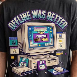 May include: A charcoal gray t-shirt featuring a graphic of a vintage computer monitor displaying the text "YOU'VE GOT MAIL" and "OFFLINE WAS BETTER" at the top. The design includes icons for Netscape Navigator, AIM Chat, a floppy disk, and a dial-up modem.