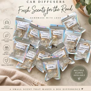 Pode incluir: Uma coleção de pequenos frascos difusores de carro em vidro com tampas de madeira e cordões, embalados individualmente em bolsas prateadas holográficas. As etiquetas nas bolsas exibem nomes de aromas como alecrim, tea tree, baunilha, sândalo, cravo, ylang ylang, cedro, eucalipto, lavanda e rosa.