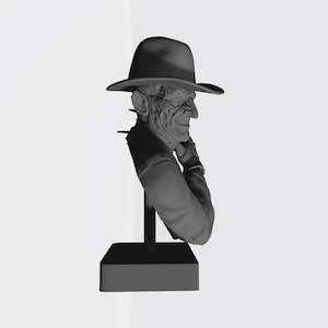 May include: A monochromatic gray bust sculpture depicting a figure with a scarred, textured face wearing a wide-brimmed fedora hat. The figure is shown from the chest up, positioned on a vertical support rod attached to a solid rectangular base.