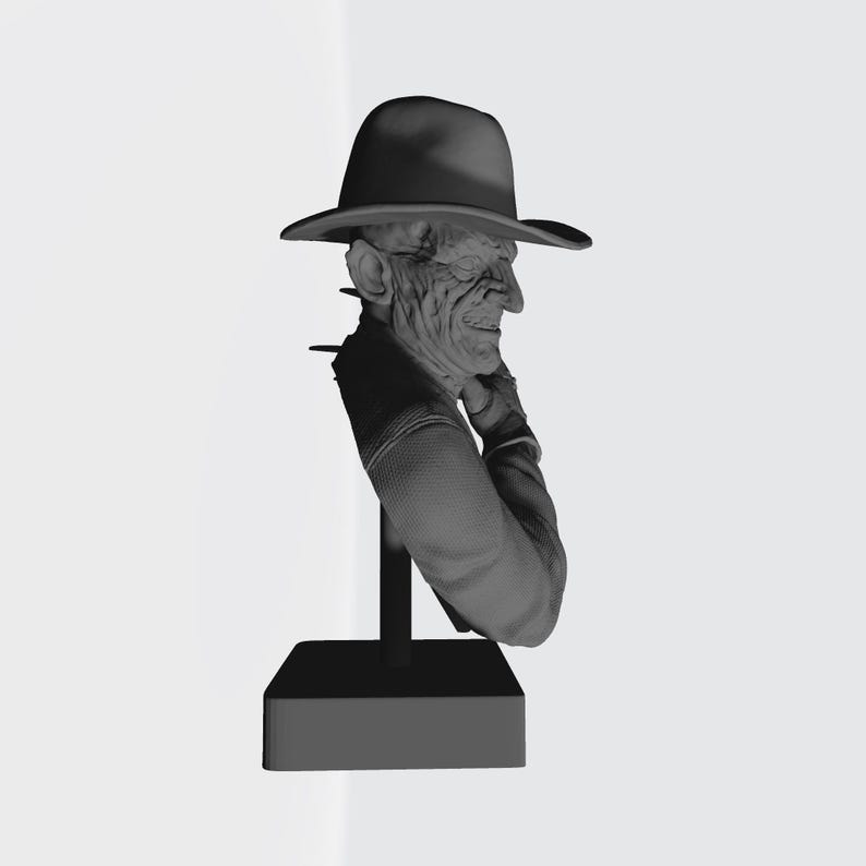 May include: A monochromatic gray bust sculpture depicting a figure with a scarred, textured face wearing a wide-brimmed fedora hat. The figure is shown from the chest up, positioned on a vertical support rod attached to a solid rectangular base.
