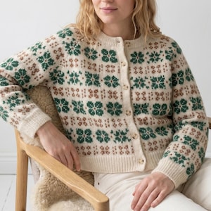 Puede incluir: Rebeca color crema con un estampado floral en verde y marrón. El suéter con botones tiene mangas largas y cuello redondo. El diseño floral se repite en la parte delantera y las mangas.