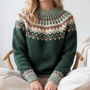 May include: A green sweater with a patterned yoke and cuffs. The yoke features a design in brown and cream colors. The sweater has a ribbed collar and cuffs. The model is wearing the sweater while sitting in a wooden chair.