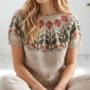Può includere: Un maglione beige a maniche corte con scollo tondo. Il maglione presenta un motivo floreale in rosso, verde e grigio. Il design include rose e foglie stilizzate. La maglia ha orlo e polsini a coste, offrendo uno stile classico e confortevole.