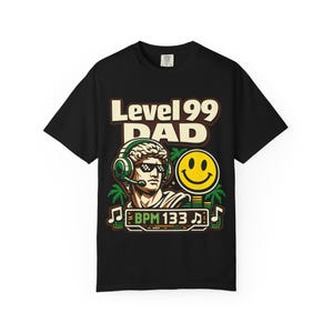 Peut inclure: T-shirt noir avec un motif graphique. Le motif comprend un buste portant un casque et des lunettes de soleil, un smiley et le texte "Level 99 DAD" et "BPM 133". Le style est rétro et numérique.