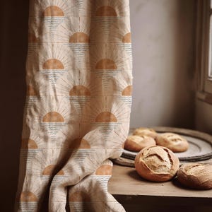 May include: A beige fabric curtain featuring a repeating pattern of orange suns with radiating lines above blue wavy water lines. The fabric is draped vertically, displaying a consistent grid of sun and sea motifs across the entire visible surface area.