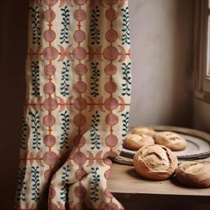 May include: A cream-colored fabric curtain featuring a repeating pattern of pink circular shapes, crescent moon motifs, and vertical teal leaf-like vines. The textile hangs vertically, displaying a structured geometric design with earthy tones.