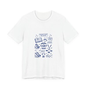 Può includere: T-shirt bianca con un design grafico blu con illustrazioni a tema hockey. Il design include una maglia con il numero 13, pattini, una mazza da hockey, un disco e il testo "Reader's Game Day Notes".
