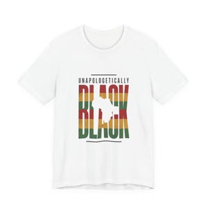 Op de afbeelding: Wit T-shirt met de tekst "UNAPOLOGETICALLY BLACK" in zwart, rood, geel en groen. Het woord "BLACK" is verticaal gestapeld met een silhouet van een continent in het midden.