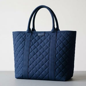 May include: A navy blue quilted tote bag featuring a diamond-stitched pattern, two sturdy top handles, and a rectangular fabric patch centered near the top opening. The bag has a structured base and vertical fabric strips extending from the handles.