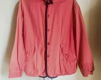 May include: A coral-colored hooded jacket with a button-up front and two front pockets. The jacket has a drawstring at the bottom and navy blue trim along the edges and hood. The jacket is hanging on a wire hanger.