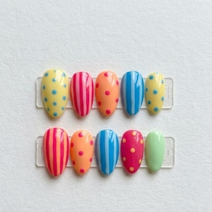 May include: A set of ten almond-shaped press-on nails arranged in two rows on clear plastic strips. The nails feature vibrant, multi-colored designs including vertical stripes and polka dots in shades of yellow, pink, orange, blue, and green.