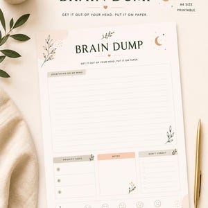 Peut inclure: Bloc-notes imprimable au format A4 "Brain Dump" avec le texte "Brain Dump" et "Get it out of your head. Put it on paper." Le bloc-notes comprend des sections pour les tâches prioritaires, les notes et le suivi de l'humeur, avec un stylo doré et une bougie allumée en arrière-plan.