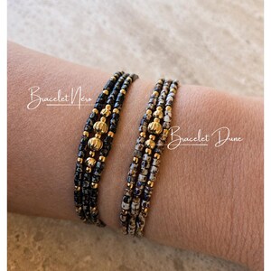 Peut inclure: Deux bracelets de perles, l'un noir et or, l'autre moucheté d'accents dorés, sont présentés sur un poignet. Les bracelets sont étiquetés "Bracelet Nero" et "Bracelet Dune" en écriture cursive. Les bracelets sont faits de petites perles.