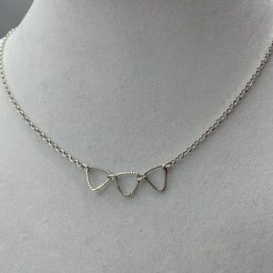 May include: A silver necklace with a chain and three connected triangular pendants.