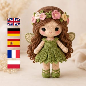 Puede incluir: Una muñeca de hada de ganchillo hecha a mano con cabello castaño, una corona floral y un vestido verde. La muñeca tiene grandes ojos negros, mejillas rosadas y delicadas alas. El hada lleva zapatos verdes con correas entrecruzadas. La muñeca mide aproximadamente 20 cm de altura.
