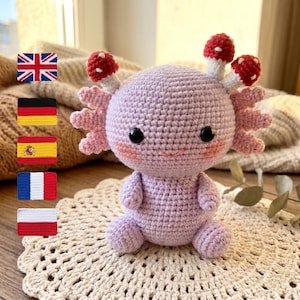May include: A handmade crochet axolotl doll in shades of lavender and pink, with red and white mushroom accents. The amigurumi creature has black safety eyes and a smiling mouth. It sits on a cream-colored, crocheted doily.