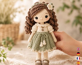 Könnte beinhalten: Eine handgefertigte Häkelpuppe mit braunen Locken, einem cremefarbenen Oberteil und einem grünen Rock. Die Puppe hat ein Blumen-Haaraccessoire und trägt braune Schuhe. Die Puppe wird von einer Hand gehalten.