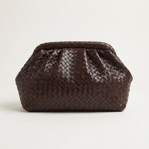 Puede incluir: Un bolso de mano de color marrón oscuro con exterior de cuero trenzado, marco redondeado estructurado y cierre superior fruncido. El bolso presenta un patrón de tejido de cesta complejo y uniforme en toda la superficie exterior.