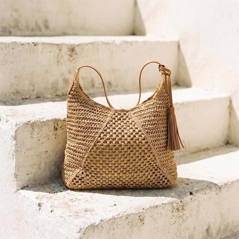 May include: A woven tote bag in a natural beige color, featuring a geometric pattern. The bag has brown leather handles and a matching tassel. The bag is sitting on a white concrete staircase.