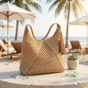 May include: A woven straw shoulder bag with leather handles and a tassel. The bag has a geometric open weave design and is set on a stone surface with a beach scene in the background.