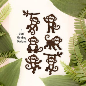 Puede incluir: Ocho diseños de monos marrón oscuro en varias poses, incluyendo colgados de una rama, sosteniendo un corazón y caminando. También está presente el texto "8 Cute Monkey Designs". Los monos están sobre un fondo blanco con follaje verde.