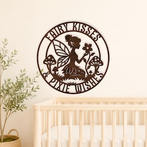 May include: A dark brown wooden sign with the words "Fairy Kisses Pixie Wishes" encircling a fairy illustration. The fairy is holding a flower, surrounded by mushrooms. The sign is circular and mounted on a white wall.