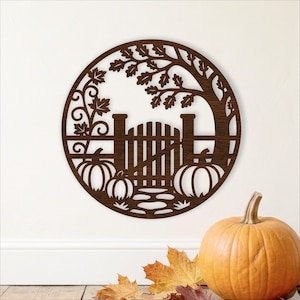 May include: A circular dark brown wooden wall art piece featuring a laser-cut design of a garden gate, a tree with leaves, and three pumpkins. The intricate cutout depicts a fence, a path, and autumn foliage within a circular frame.