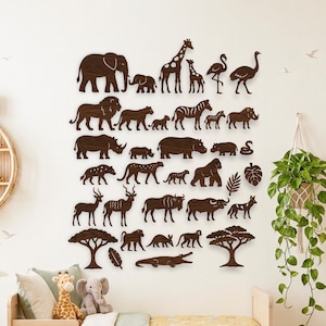 Könnte beinhalten: Eine Sammlung von Wandaufklebern aus dunkelbraunem Holz, die Silhouetten verschiedener afrikanischer Tiere zeigen, darunter ein Elefant, eine Giraffe, ein Löwe, ein Zebra, ein Nashorn, ein Flusspferd, ein Gorilla und ein Krokodil sowie zwei Bäume.