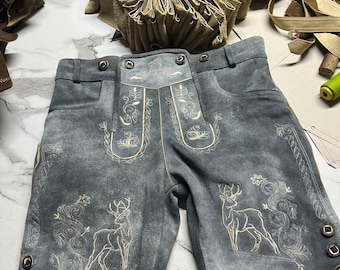Könnte beinhalten: Graue Lederhose aus Wildleder mit detaillierter cremefarbener Stickerei von Hirschen und floralen Motiven auf den Vorderteilen. Die Hose verfügt über einen Bund mit Gürtelschlaufen, seitliche Metallknöpfe und einen verzierten Latz vorne.