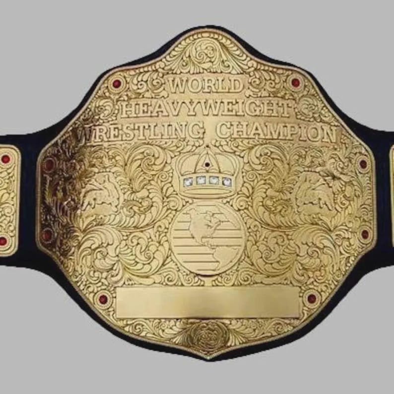 Puede incluir: Un cintur&oacute;n de campeonato de lucha libre dorado con grabados intrincados de volutas, un emblema de corona central y un gr&aacute;fico de globo terr&aacute;queo. El texto dice WORLD HEAVYWEIGHT WRESTLING CHAMPION. El cintur&oacute;n incluye peque&ntilde;os acentos circulares rojos y una correa negra.