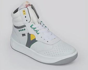 Puede incluir: Zapatilla alta blanca con detalles grises, amarillos y verdes. La zapatilla presenta una suela blanca gruesa y la palabra "Serma" es visible en la lengüeta. La zapatilla tiene cierre de cordones y un cuello acolchado.