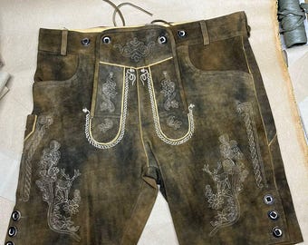 Könnte beinhalten: Braune Lederhose mit dekorativer Stickerei. Die Hose hat detaillierte Nähte, Taschen und Knopfverschlüsse. Die Stickerei umfasst Blumen- und Hirschmotive mit hellfarbenem Faden. Die Hose hat ein Vintage-Aussehen.