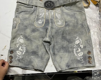 Könnte beinhalten: Graue Lederhose mit weißer Blumenstickerei und dekorativen Knöpfen. Die Hose hat einen passenden Gürtel mit detaillierter Schnalle. Zusätzliche Ledergürtel sind im Hintergrund zu sehen.