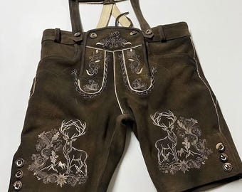 Könnte beinhalten: Dunkelbraune Lederhose mit cremefarbener Stickerei, die Hirsche, florale Motive und Berglandschaften zeigt. Die Hose verfügt über verstellbare Träger mit Metallschnallen, einen Latz sowie dekorative Metallknöpfe an den Beinabschlüssen.