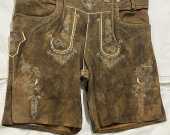 Könnte beinhalten: Braune Lederhose mit heller Zierstickerei auf den Vorderteilen, zwei Seitentaschen, einer kleinen Seitentasche, Gürtelschlaufen und Metallknöpfen am Bund sowie einer Schnürung an der Rückseite des Hosenbundes.