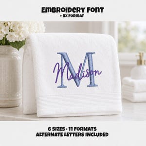May include: A white terry cloth towel featuring an embroidered design with a large light blue letter M and the name Madison in purple script. The text EMBROIDERY FONT + BX FORMAT and 6 SIZES 11 FORMATS ALTERNATE LETTERS INCLUDED is visible.