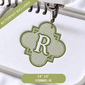 Puede incluir: Un diseño de bordado a máquina verde oliva con forma de cuatrifolio, fondo cuadriculado y la letra R en el centro. El diseño está bordado sobre tela blanca dentro de un bastidor gris. El texto dice BX FORMAT INCLUDED.
