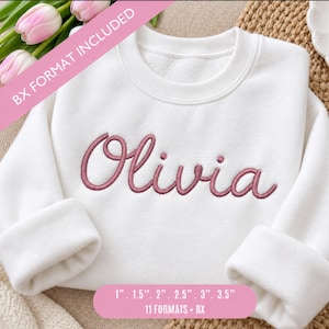 Puede incluir: Una sudadera blanca de cuello redondo con el nombre Olivia bordado en una fuente cursiva de color rosa empolvado en el pecho. La imagen incluye el texto BX FORMAT INCLUDED y enumera los tamaños 1", 1.5", 2", 2.5", 3", 3.5", 11 formatos y BX.