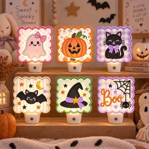 May include: A set of six square Halloween-themed night lights with scalloped edges. Designs include a pink ghost with a bow, an orange pumpkin, a black cat with a purple bow, a black bat, a black witch hat, and the word Boo with a spider.