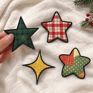 May include: Four fabric star-shaped patches with black embroidered edges. One is green plaid with a small tree, one is red and white plaid, one is a four-pointed yellow star with small orange stars, and one is a patchwork of red, green, and orange.