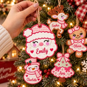 May include: A set of five embroidered felt Christmas ornaments featuring a Santa Claus, a reindeer, a gingerbread person, a snowman, and a Christmas tree. Each ornament is decorated with pink and white patterns and personalized names.