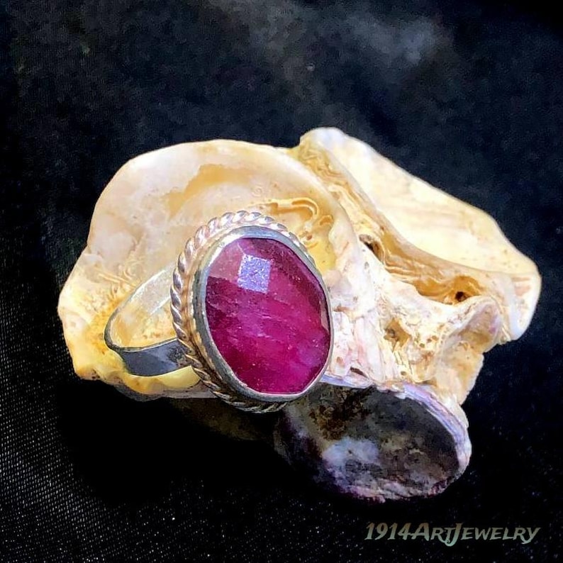 Handmade sterling silver ruby ring featuring an oval faceted ruby gemstone surrounded by a vintage rope-style bezel setting.