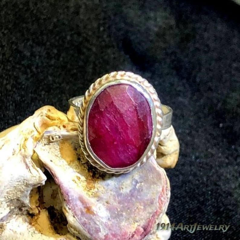 Handmade sterling silver ruby ring featuring an oval faceted ruby gemstone surrounded by a vintage rope-style bezel setting.