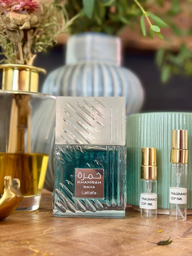 May include: A square glass perfume bottle with a textured surface and a silver cap, labeled Khamrah Waha Lattafa, accompanied by two small clear sample vials with gold caps labeled Fragrance EDP 3ML and Fragrance EDP 5ML respectively.