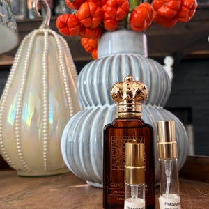May include: A rectangular amber glass perfume bottle with a gold crown-shaped cap, accompanied by two small clear glass sample vials with gold spray nozzles. The labels on the vials read FRAGRANCE EDP 3ML and FRAGRANCE EDP 5ML respectively.